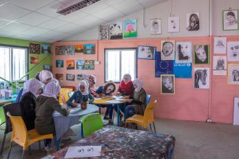 Young people sit together in a classroom decorated with drawings and paintings.