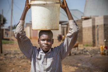 Nigerian boy transporting a bucket on his head.