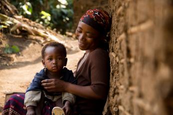 An adult sits against a wall with a child on their lap.