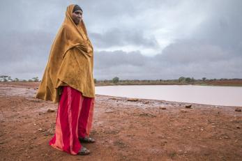 An adult stands on the shore of a body of water.