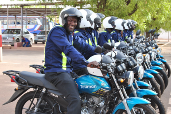 A group of motorcycle taxis and their drivers lineup in a row.