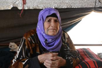 An elderly adult sits with their hands clasped. 