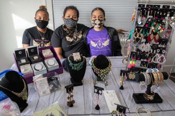 A business owner sits at a table of their wares alongside their children 