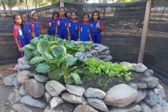 Timor leste children standing behind keyhole garden.