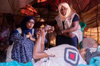 Mercy corps ceo tjada d’oyen mckenna listening to a villager seeking treatment, food, water, and shade from the hot sun in a shelter.