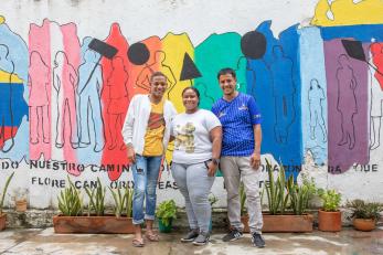 Three people posing in front of mural.