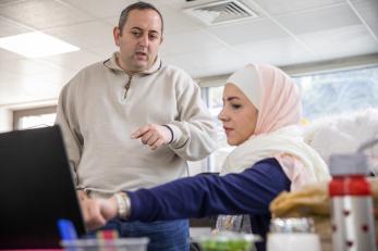 Photo shows a man and woman in conversation while looking at a computer screen.