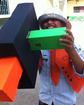 Child with cardboard camera wearing handmade mercy corps uniform