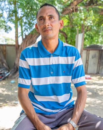 Jose sits outside in the yard with his hands folding in his lap