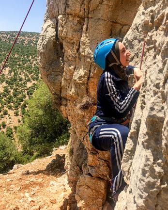 A woman wearing a harness and helmet climbs a rock face in jordan