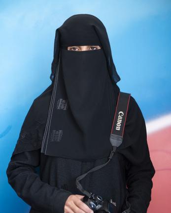 A woman holds a camera with the strap over her shoulder in yemen