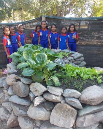 Timor leste children standing behind keyhole garden.