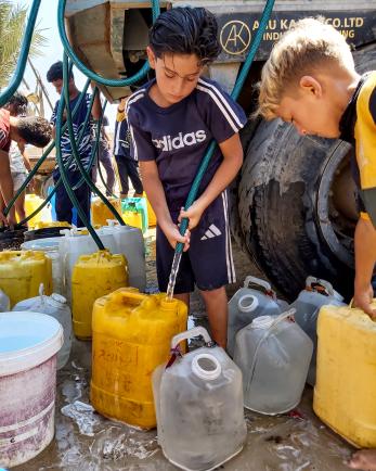 Young palestinian children filling jerrycans with potable water.