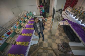 Man standing between rows of purple fabric and sewing machines