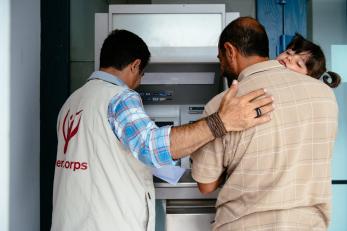 Mercy Corps team member helping a father (holding his daughter) to use an ATM