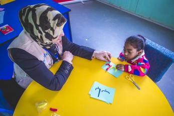 Haleema, a shadow teacher, working with Malak at a table