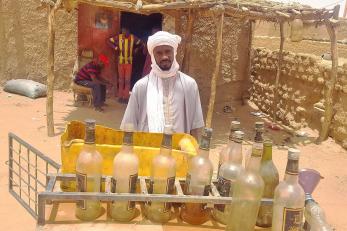 Hassan standing behind a shelf with several bottles on it