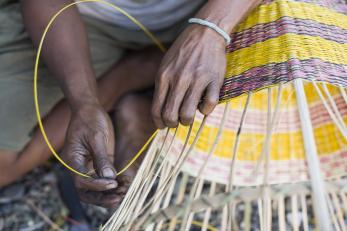 Hands weaving a yellow basket