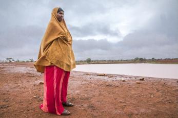 Woman dressed in dark yellow and red, standing near a body of water