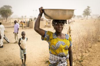 Woman carrying a large container balanced on her head, supported by her hand