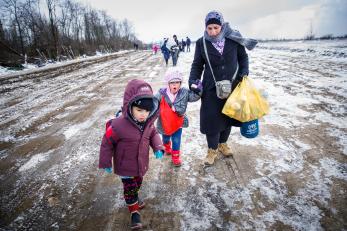 Woman with two young children walking with bags across snow-covered landscape