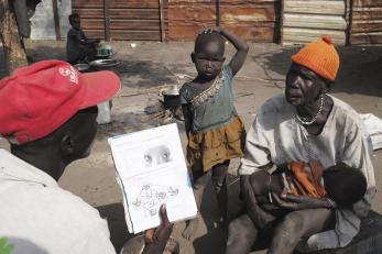 Two men talking to one another, with a child standing between them. One man is holding a baby.