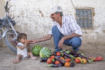 Man and baby with vegetables and fruit on the ground between them