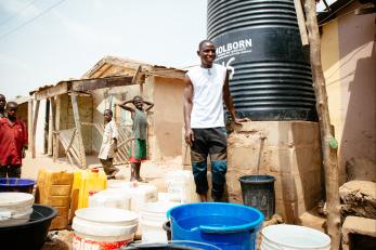 Nigerian man in front of water cistern and home.