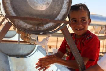 boy washing hands at refugee camp water station