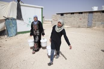 Two syrian refugees retrieving water in a camp from a water station.