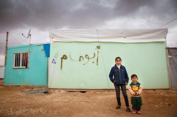 Syrian refugees - sister and brother - stand in front of a shelter.