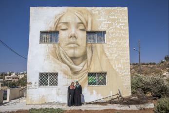 Two woman in front of a building with a large mural painted on it.