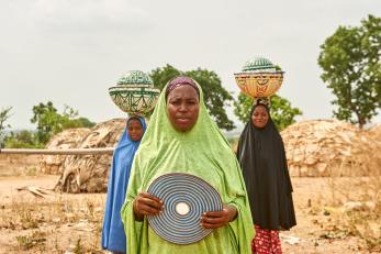 Three Nigerian woman in traditional dress; two with balanced loads on their heads.