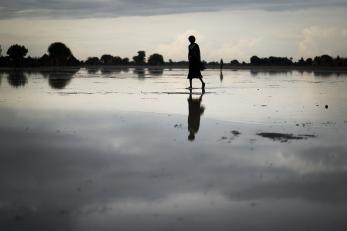 Woman walking under cloudy sky with silhouette reflected on wet ground