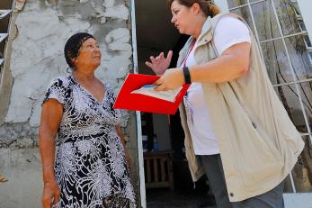A Mercy Corps team member holding a folder, paper and pen speaks to a woman in Puerto Rico