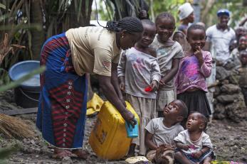 A woman pouring water for children in drc