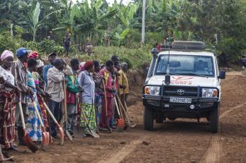 Mercy corps vehicle on a dirt road with people gathered nearby in drc