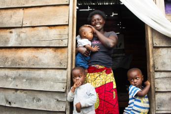 Justine stands in the doorway of her small wooden home, which is the only source of light for the tiny space built on lava rock. She and her family are grateful for the Mercy Corps tap stand across the street that brings clean water close to their home. Photo: Liz Hummer/Mercy Corps