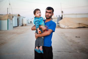 A man holds his young son, who has a peach in his hand