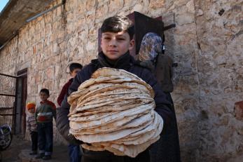 A boy holds a large stack of bread