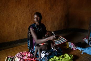 A woman holds and gently fans a baby in her lap in south sudan