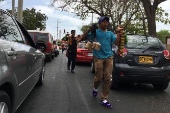 Men walk between cars at a red stoplight offering snacks for sale