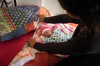 A baby wearing a hat is tucked into bed