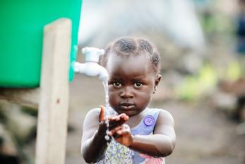 A child washes hands at a hygiene station in a displacement camp on the outskirts of Goma, DRC. In 2015, when this photo was taken, about 5,000 people lived in the camp because of ongoing violence and political instability in eastern Congo. Photo: Corinna Robbins/Mercy Corps