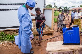 Mercy Corps supports the Malepe Health Center in DRC with chlorine and hand washing kits to disinfect hands before entering. This measure is very effective for the prevention of Ebola. Kavira, 23, pregnant with her first child, comes to the health center for an antenatal clinic. Her feet are disinfected before entering. Photo: Rudy Nkombo/Mercy Corps