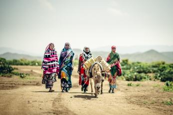 Four women in Ethiopia wearing bright colors and walking behind a donkey