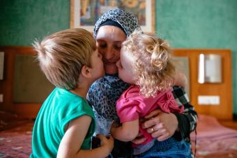 A woman receives kisses on her cheeks from a young boy and girl as she holds them tight