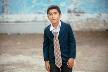 A boy wearing a jacket and button-down shirt with the top buttons open and a tie clipped to the middle of his shirt.