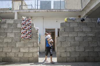 A boy in a cinderblock doorway holding a baby