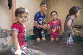 Four children play in a shallow pool filled with water